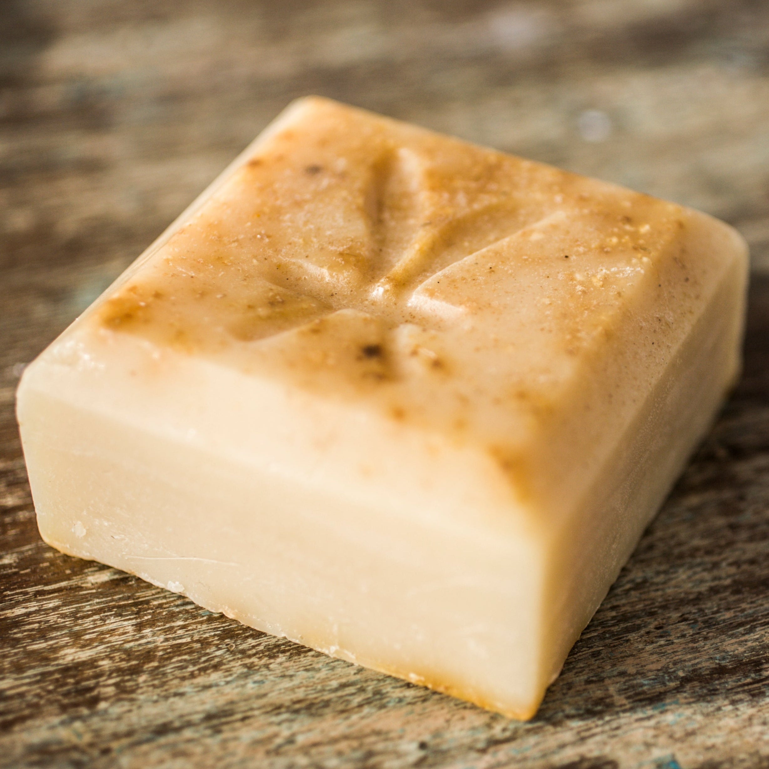 Square piece of soap with brownish discoloration on a rustic wooden surface