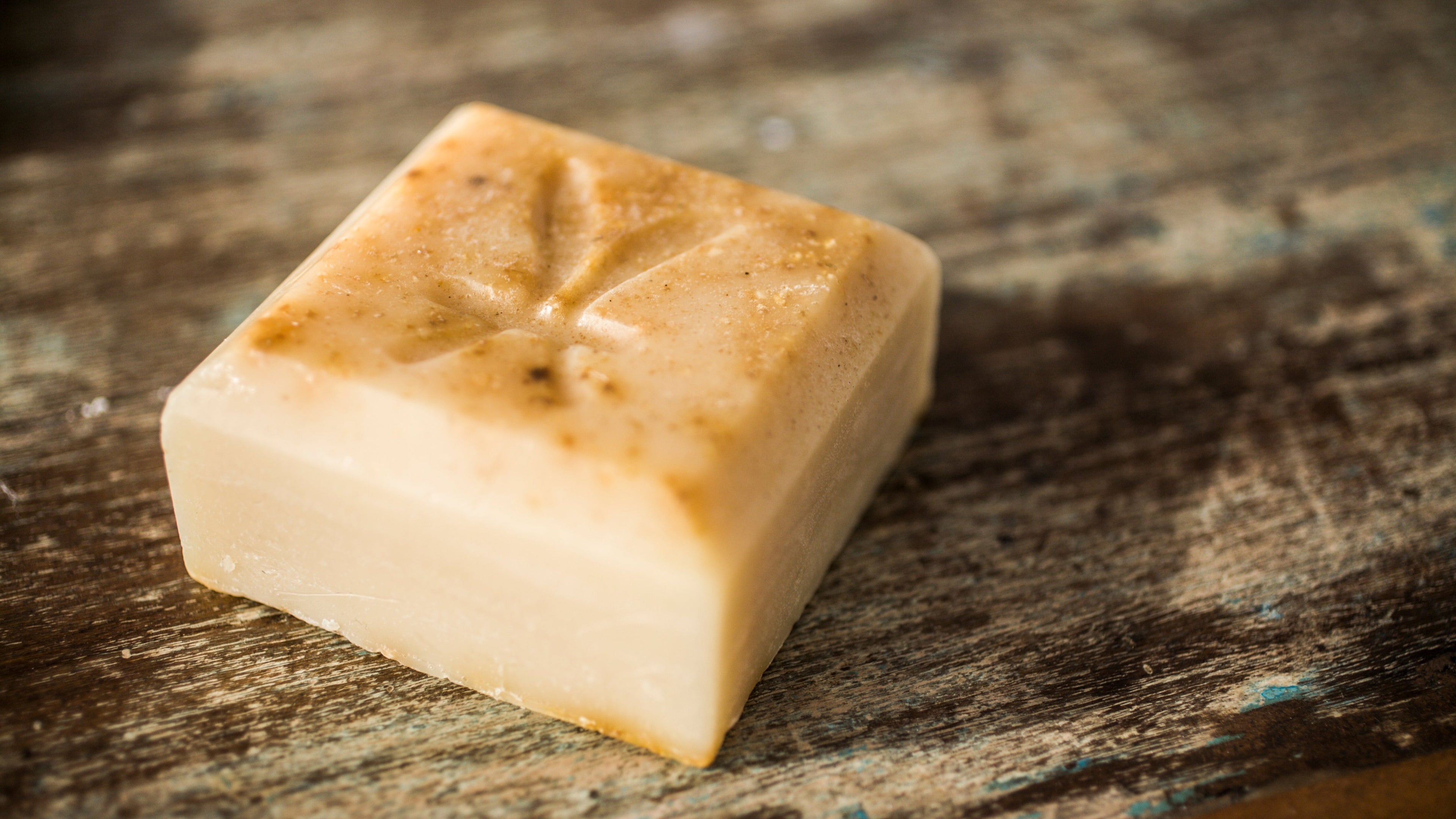 Square piece of soap with brownish discoloration on a rustic wooden surface