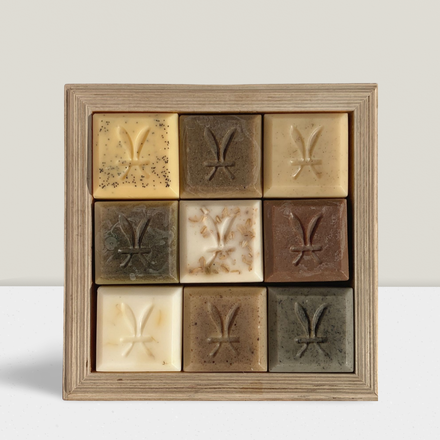 Nine square soap bars with different textures and colors arranged in a wooden frame.