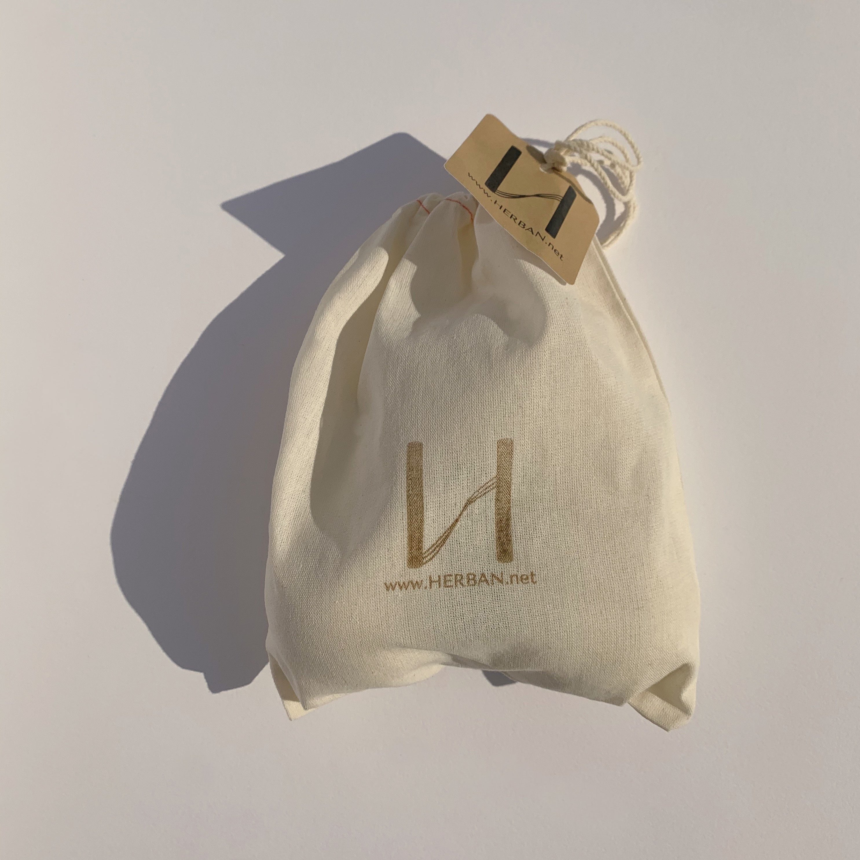 3 organic and reusable hypoallergenic wool dryer balls sit next to a bottle of Herban's linen essential oil blend in an Herban mesh bag