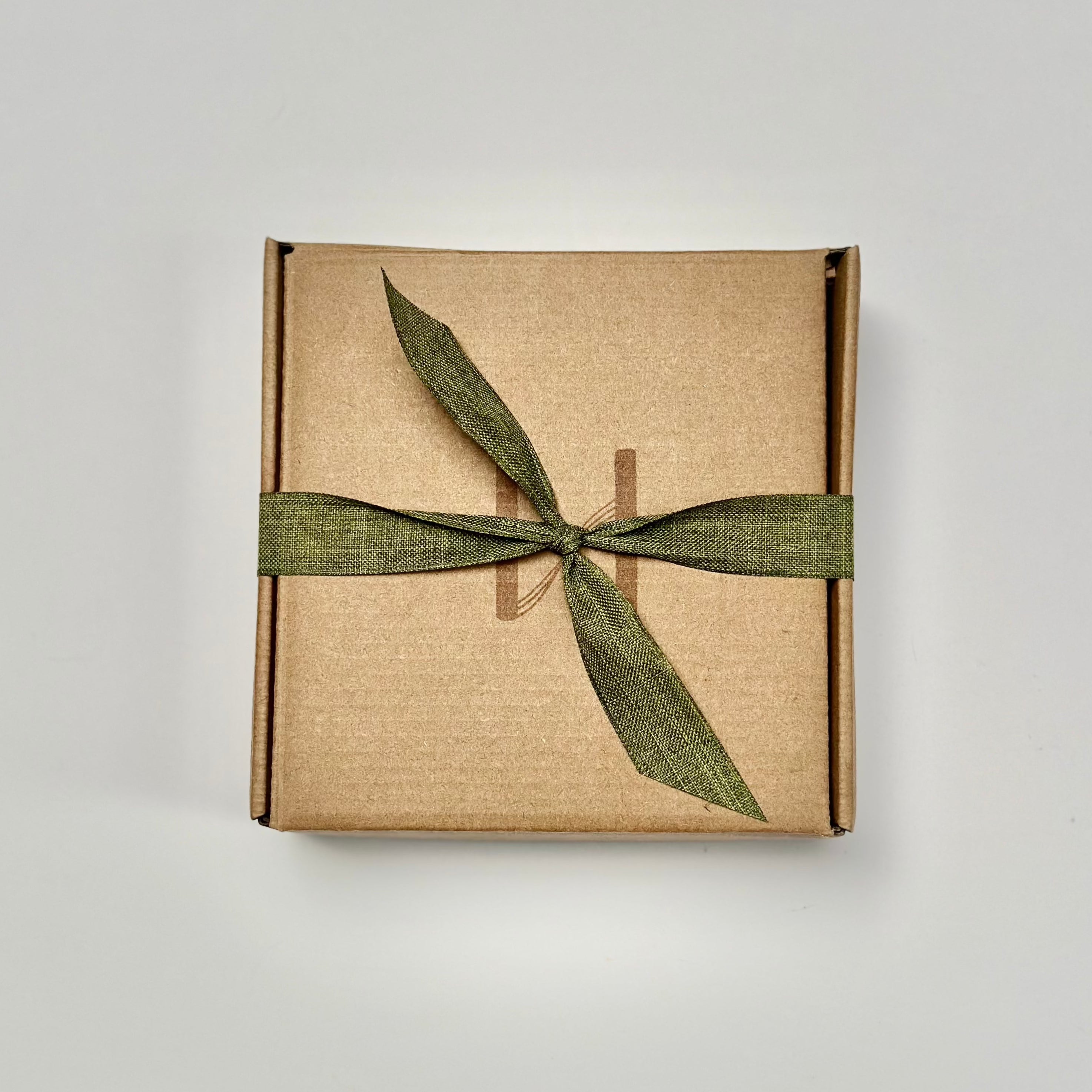 Flat kraft tuck top box closed and tied with a green linen ribbon