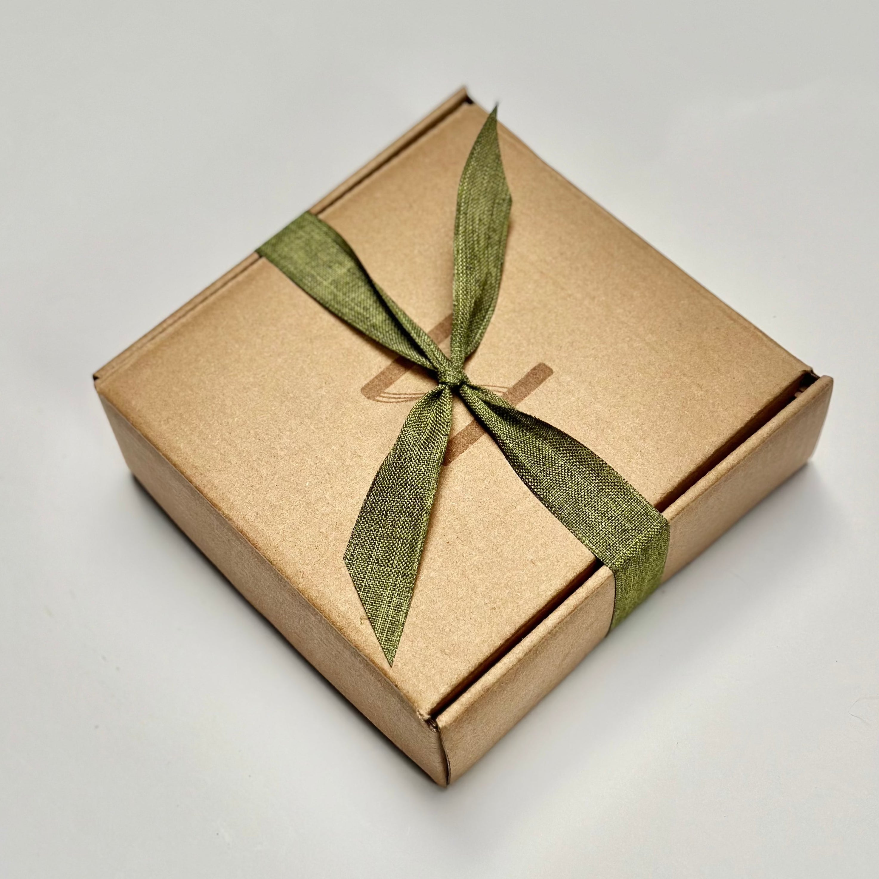 Flat kraft tuck top box closed and tied with a green linen ribbon