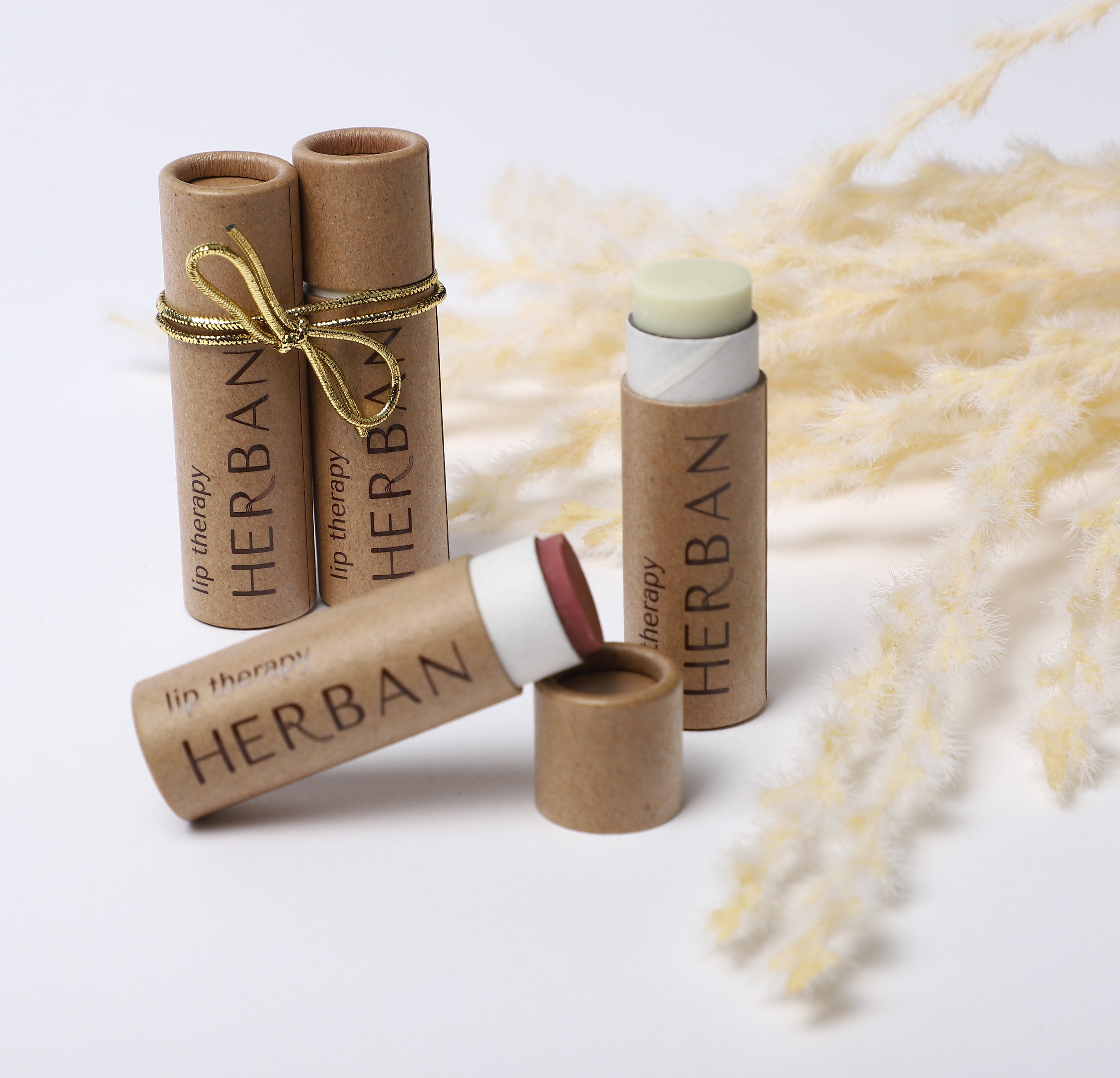 Showcasing a small collection of different varietes of Lip Therapy Lip balm made with shea butter & avocado oil and stored in plastic free, compostable packaging, complete with a small ribbon